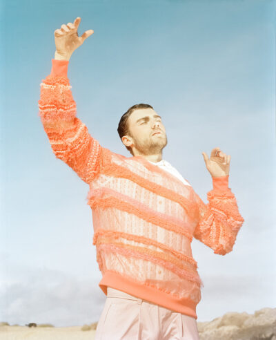 Male model stood on the beach with arms raised and eyes closed.