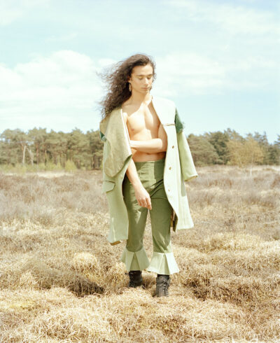 Androgynous male model stood in a dry yellow field in the middle of the forrest.