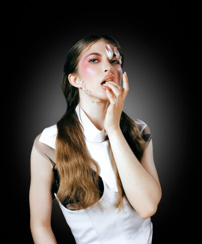 Close up portrait of a female model covered in flower petals and dressed in victorian clothing as she bites her fingers posing at the camera